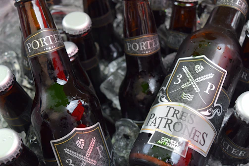 A rustic wooden crate holding a 3-pack of Quimkolla special edition beers with vibrant Andean motifs.
