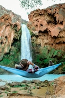 man laying on blue hammock in front of waterfalls