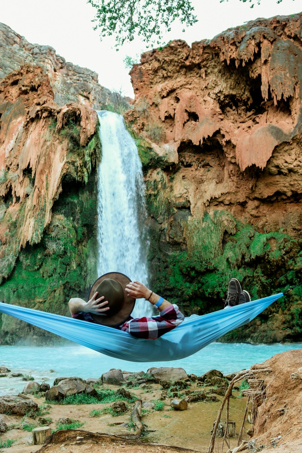 homem deitado em rede azul em frente a cachoeiras