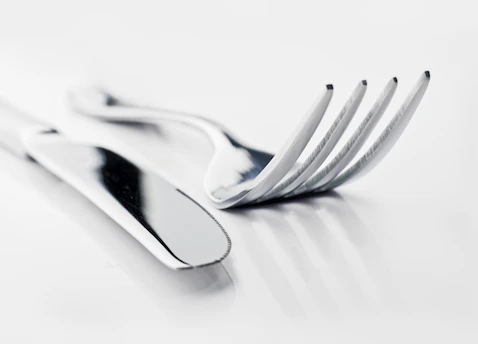 Close-up of polished stainless steel forks, knives, and spoons neatly arranged on a wooden table.