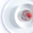 A round dessert sits in a white bowl, topped with a single fresh red strawberry. The dessert appears glazed, with a smooth white sauce pooling around it.