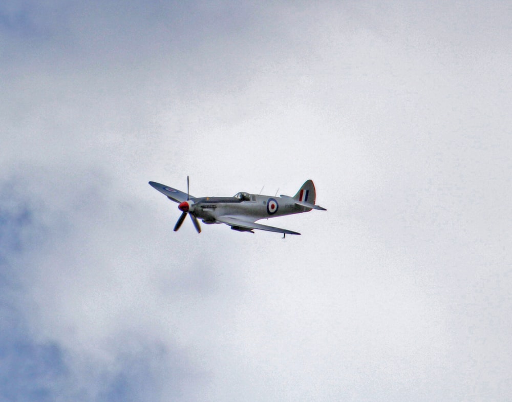 gray and red jet flying through cloudy sky