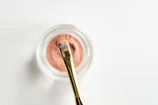 brown makeup brush in front pink powder on glass case