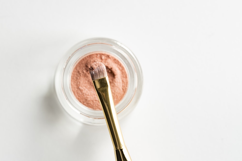 brown makeup brush in front pink powder on glass case