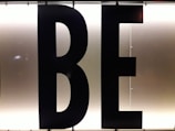 Black capital letters 'B' and 'E' against a bright, white illuminated background, possibly part of a sign or display board.