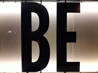 Black capital letters 'B' and 'E' against a bright, white illuminated background, possibly part of a sign or display board.
