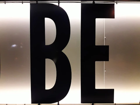 Black capital letters 'B' and 'E' against a bright, white illuminated background, possibly part of a sign or display board.