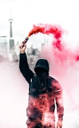person wearing black and red hoodie holding smoke bomb