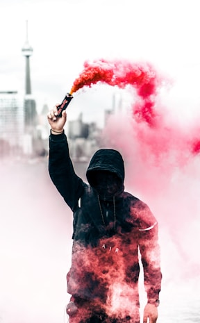 person wearing black and red hoodie holding smoke bomb