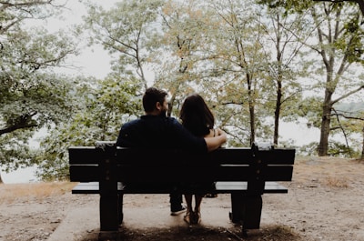 The couple sharing a quiet moment on a rustic wooden bench surrounded by autumn foliage.