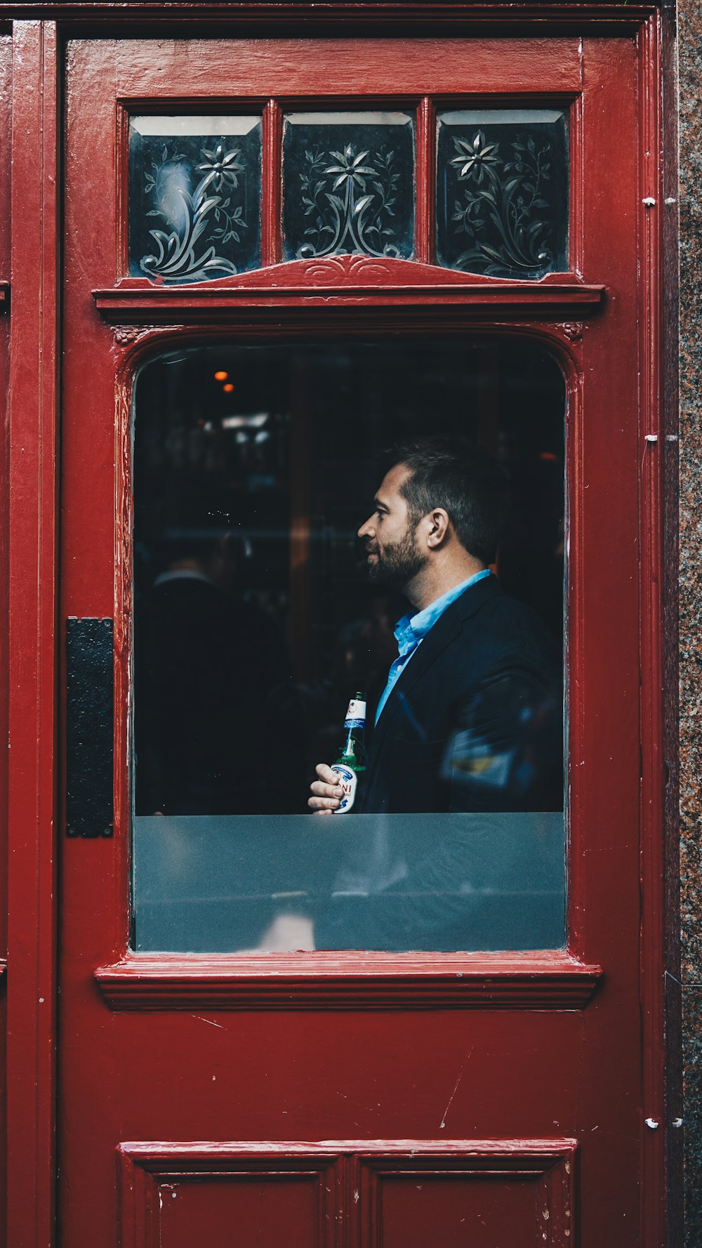 man standing beside red wooden glass door inside the building