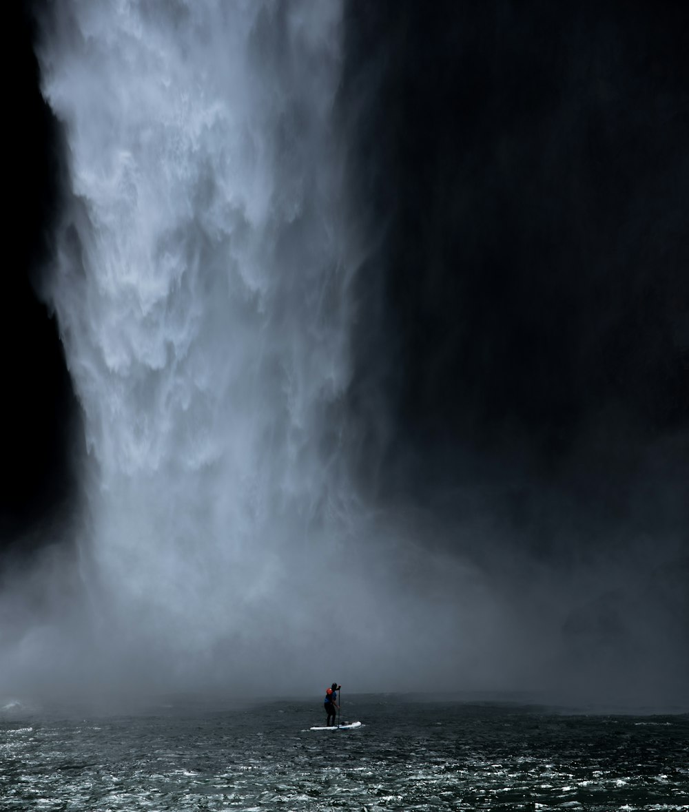 Mann im weißen Paddelbrett in der Nähe des Wasserfalls