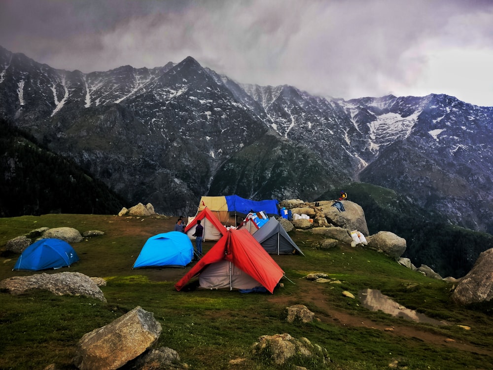 회색 하늘 아래 회색 산 근처의 푸른 잔디밭에 다양한 색상의 야외 텐트