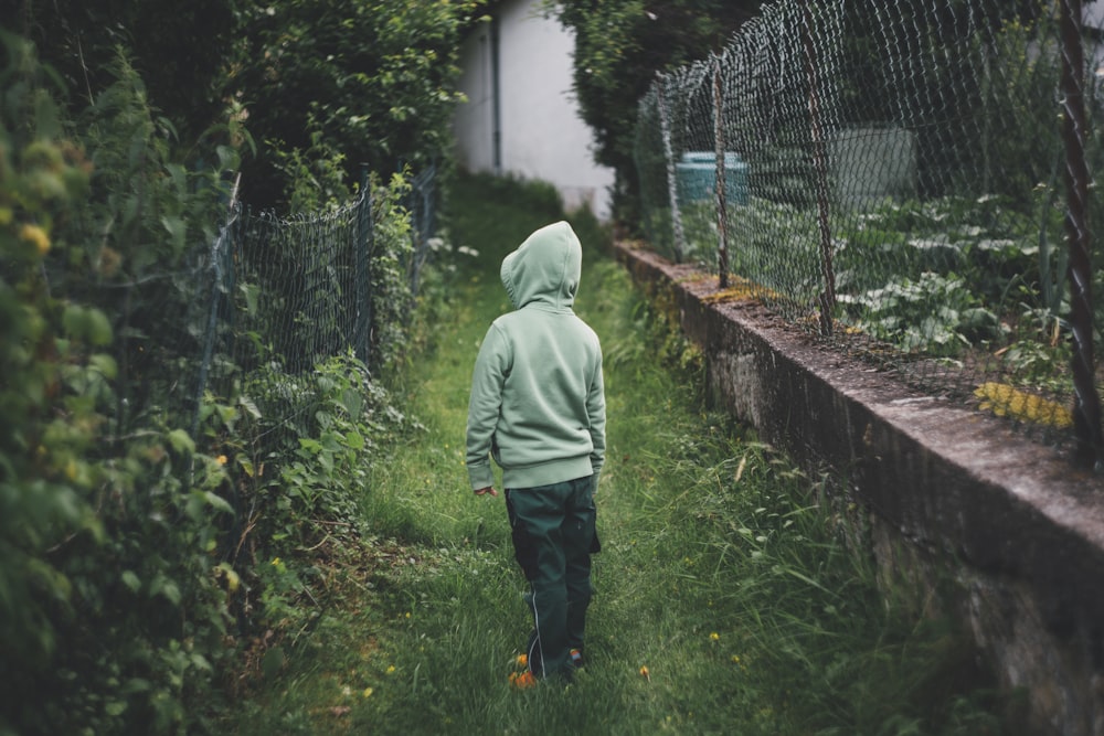 boy standing on grass and facing fence during daytime