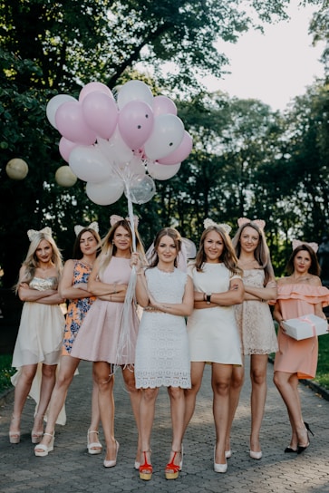 A group of diverse women wearing pink shirts, smiling and holding hands in a sunny park.