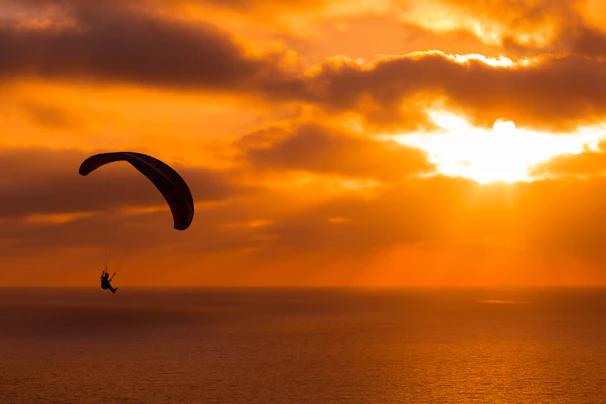 Paraglider soaring above the turquoise waters of Ölüdeniz with the sun setting in the background