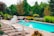 A bright, inviting backyard with a shimmering pool surrounded by lush greenery and comfortable lounge chairs.