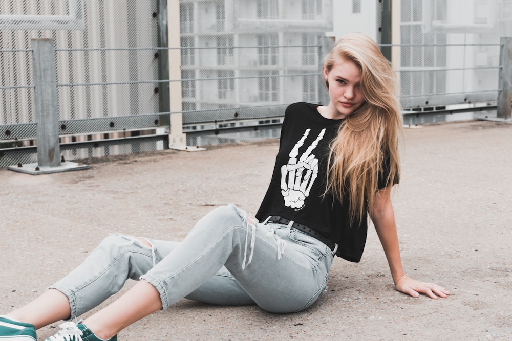 woman wearing black and white shirt and blue jeans sitting on pathway