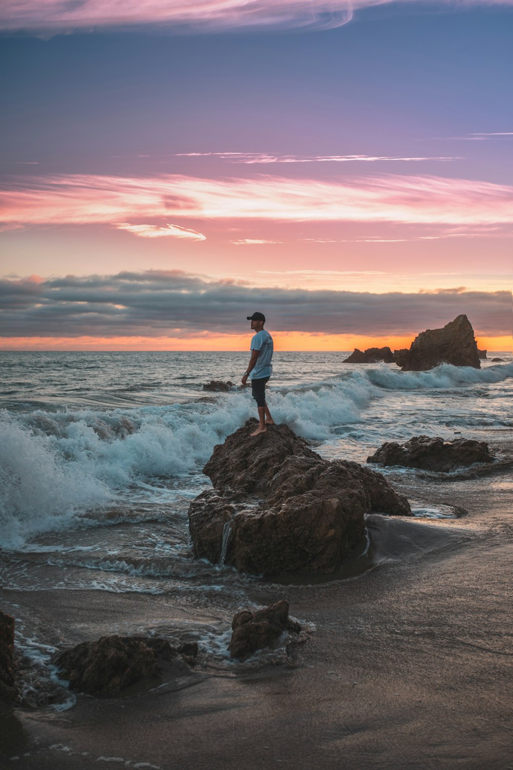 Mann, der tagsüber auf einem Felsen mit Wellen steht