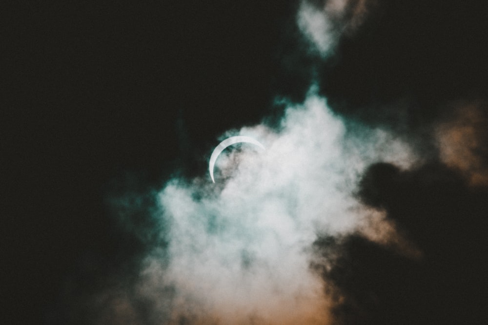 half moon hiding behind white and black clouds