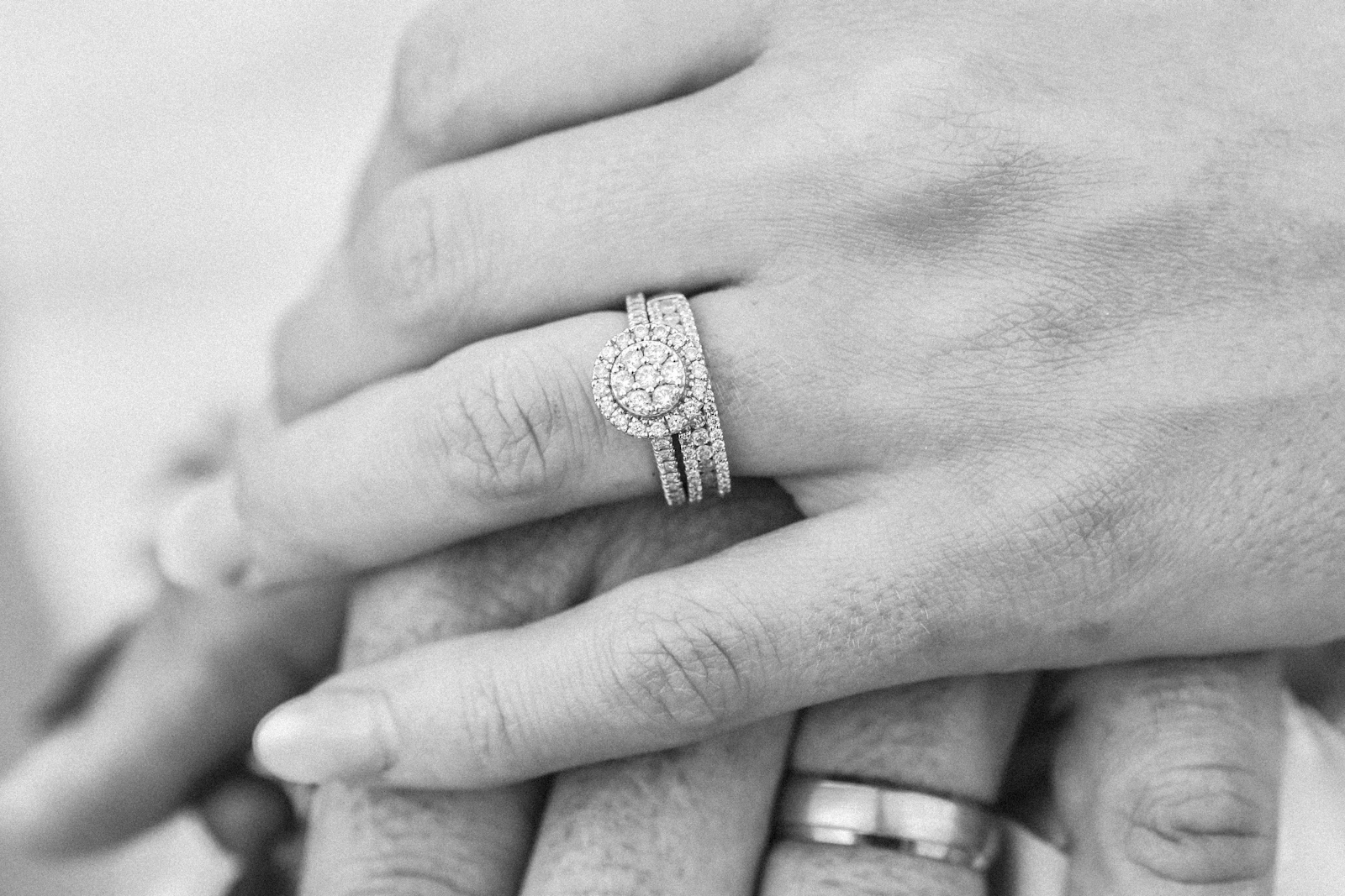 A close-up, grayscale photo of a married couple's clasped hands, wedding rings visible