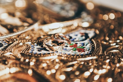 Intricate gold jewelry serves as a detailed background with ornate engravings, featuring two elegant gold rings placed prominently at the center.