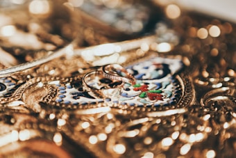 Intricate gold jewelry serves as a detailed background with ornate engravings, featuring two elegant gold rings placed prominently at the center.