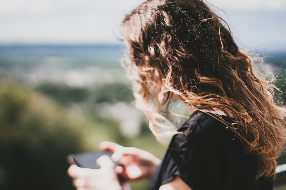 Frau mit langen lockigen blonden Haaren mit Smartphone