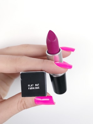 Close-up of a hand holding a vibrant lipstick from Beauty Supply.