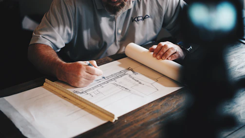 A professional advisor reviewing building plans on a construction site with a calm and focused expression.