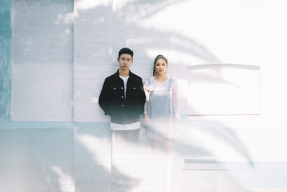 minimalist photography of man beside woman while leaning against wall
