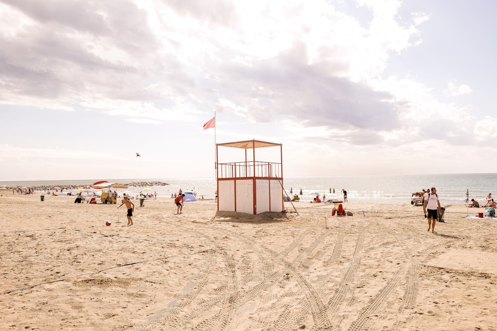 Weißer und roter hölzerner Rettungsschwimmerturm, der tagsüber von Menschen in der Nähe des Ozeans umgeben ist