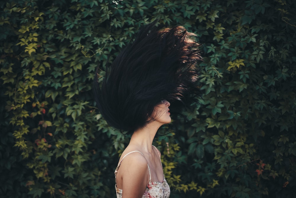緑の葉の壁の前で髪を振る女性