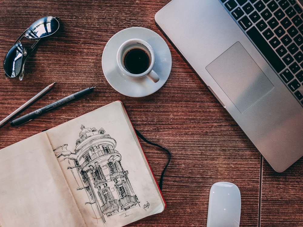 white ceramic mug beside silver laptop computer and book