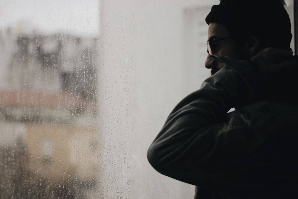 man touching neck while looking outside glass window