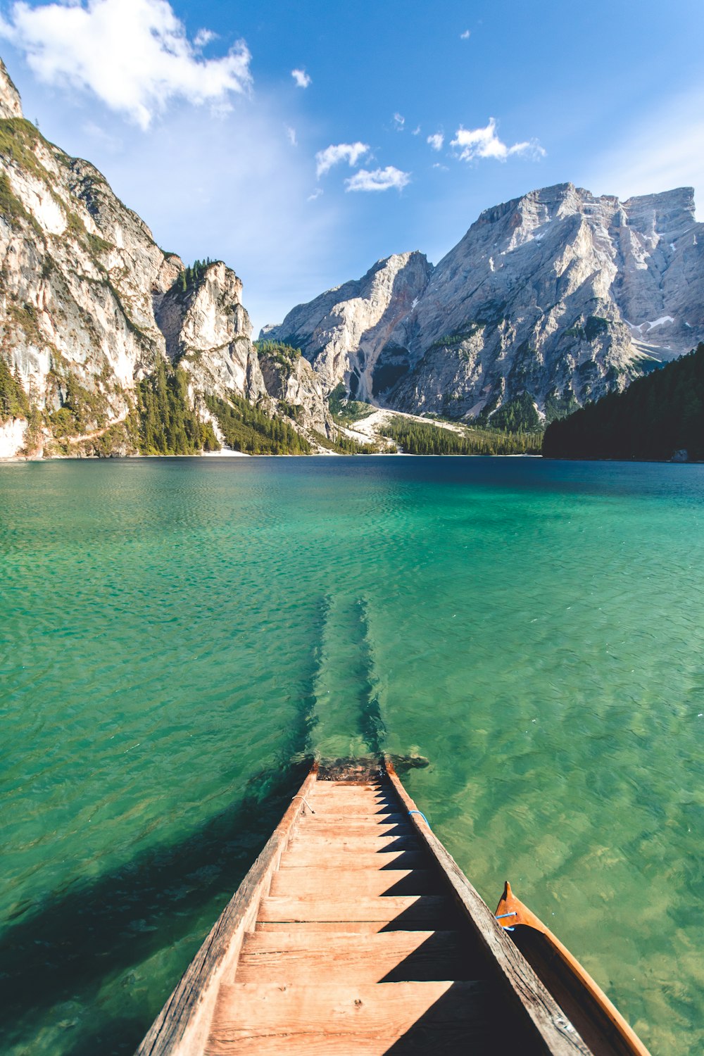 braune Holzleiter aus Holz im Wasser mit felsigem Berg vor sich unter weißem und blauem Himmel