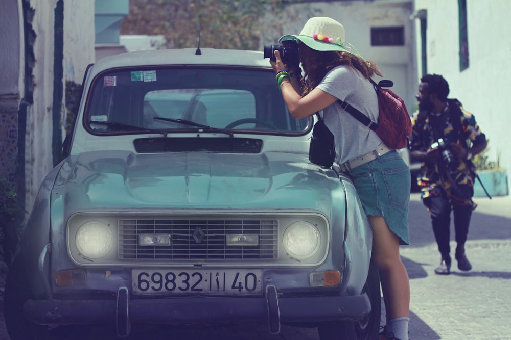 woman in black and red jacket leaning on green car