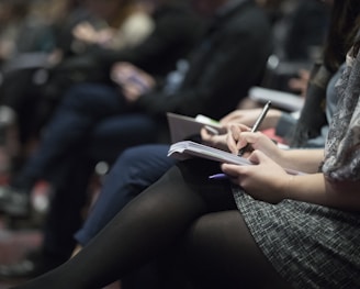 selective focus photography of people sitting on chairs while writing on notebooks