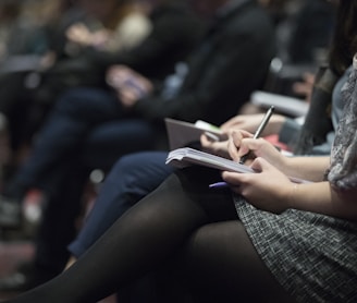 selective focus photography of people sitting on chairs while writing on notebooks