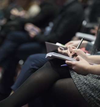 selective focus photography of people sitting on chairs while writing on notebooks