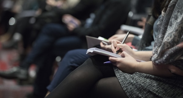 selective focus photography of people sitting on chairs while writing on notebooks