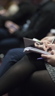 selective focus photography of people sitting on chairs while writing on notebooks