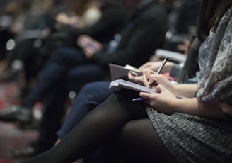 selective focus photography of people sitting on chairs while writing on notebooks