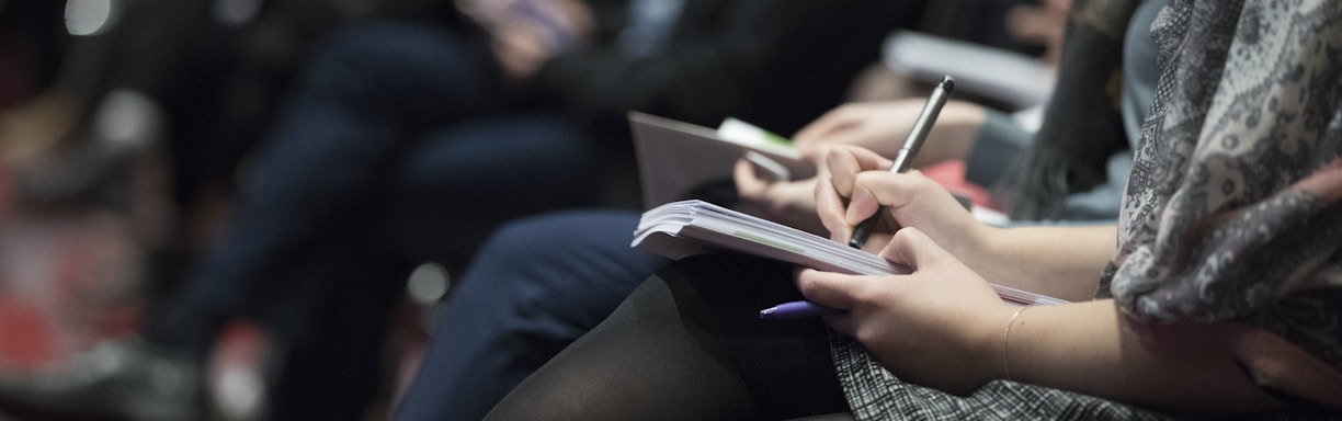 selective focus photography of people sitting on chairs while writing on notebooks