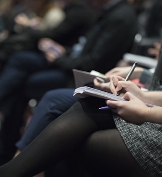 selective focus photography of people sitting on chairs while writing on notebooks