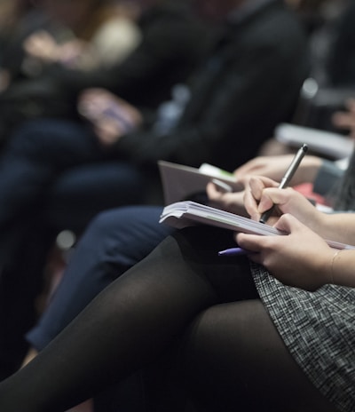 selective focus photography of people sitting on chairs while writing on notebooks