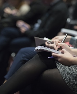 selective focus photography of people sitting on chairs while writing on notebooks