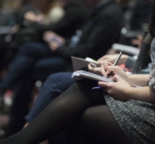 selective focus photography of people sitting on chairs while writing on notebooks