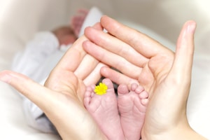 person holding baby's toe with yellow petaled flower in between