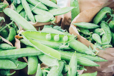 Sachets and tins of green peas and broad beans displayed on a rustic wooden surface.